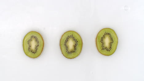 Water-splashes-in-slow-motion.-Top-view:-three-pieces-of-kiwi-washed-with-water-on-a-white-background